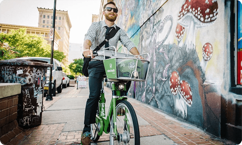A man ridding a green bike down town